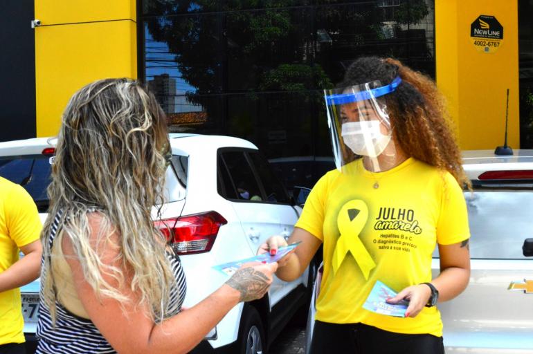 mulher com camisa da camapanha julho amarelo entregando panfleto para outra mulher 