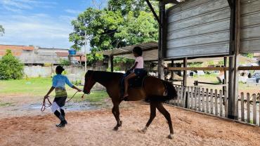 criança andando a cavalo sob a supervisão de um adulto 