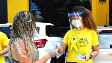 mulher com camisa da camapanha julho amarelo entregando panfleto para outra mulher 
