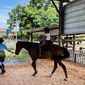 criança andando a cavalo sob a supervisão de um adulto 